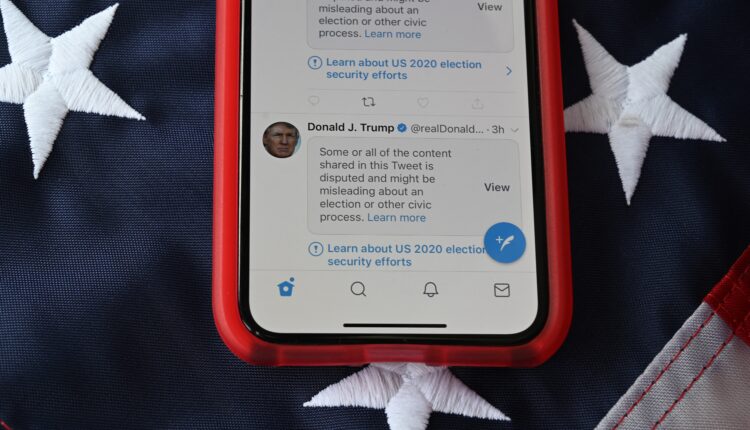 Teléfono móvil colocado en una bandera de los Estados Unidos con Tweets del presidente de los Estados Unidos, Donald Trump, enmascarados con advertencias impuestas por Twitter.