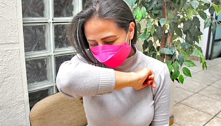 Mujer que utiliza cubrebocas se cubre con el antebrazo para estornudar.