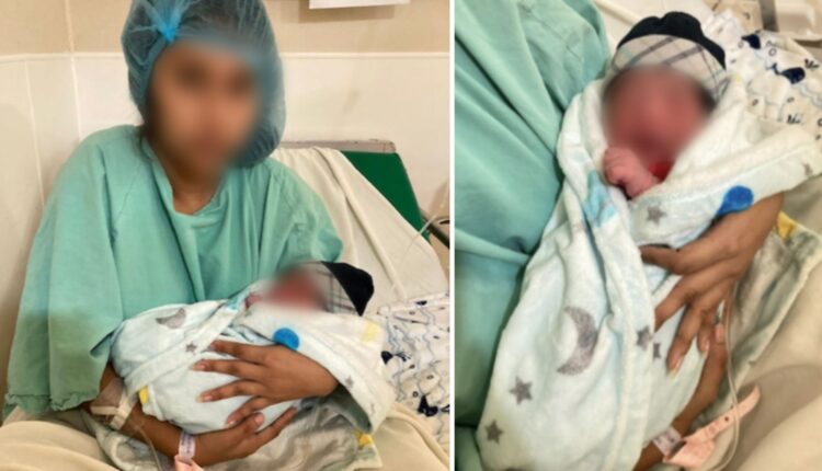 Una madre que viste una bata verde en el hospital y se encuentra sentada en una camilla, sostiene en sus brazos a su hijo después del parto.